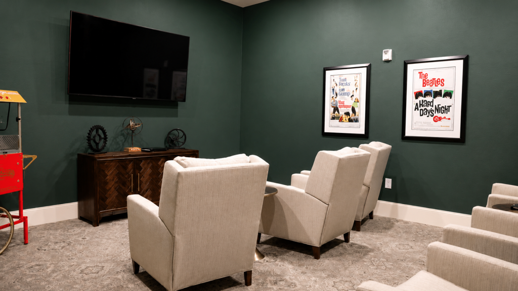 Theater lounge with wall-mounted television, upholstered chairs, and vintage movie posters